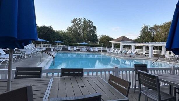 Un área junto a la piscina con sillones de descanso y sombrillas, una terraza de madera y una vista despejada de la piscina.