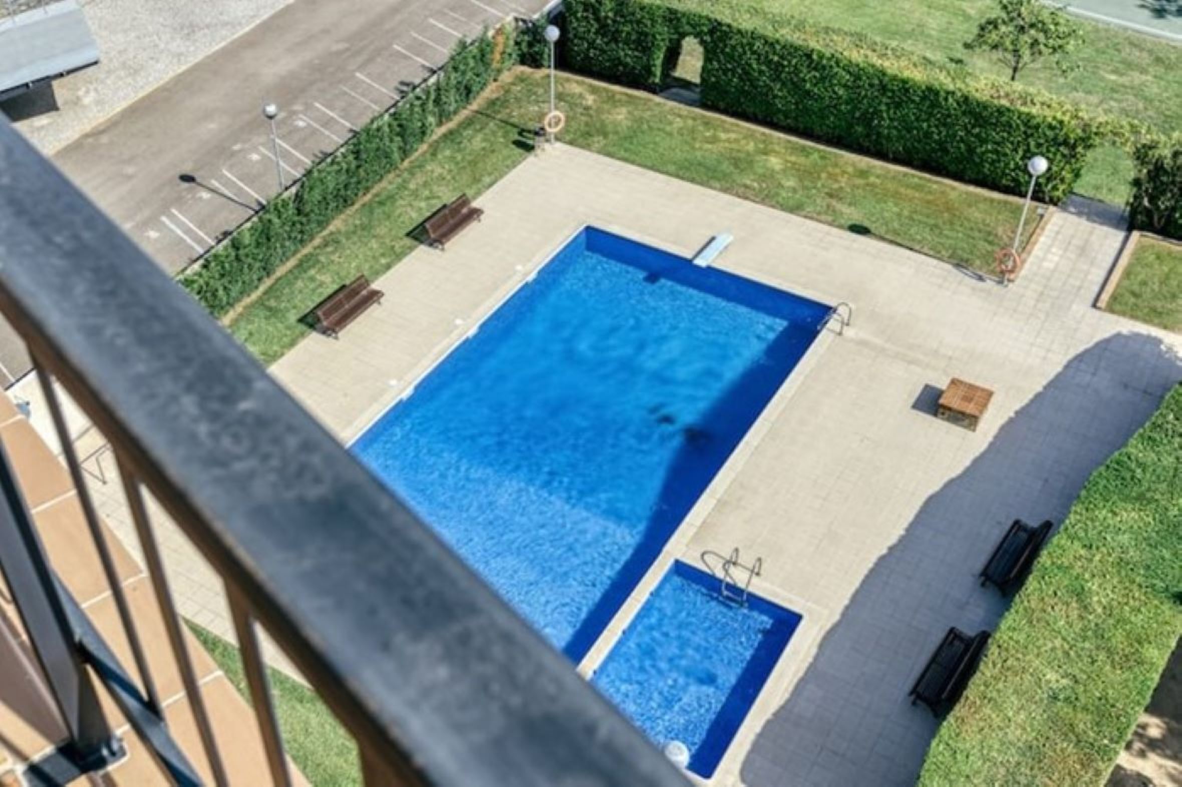 Vista aèria d'una piscina rectangular amb un petitet jacuzzí adjacent, envoltada per un solàrium pavimentat, amb bancs i una tanca.