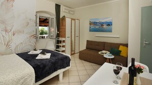A bedroom with a bed, a small table with wine glasses, a sofa, and a painting of a lake.