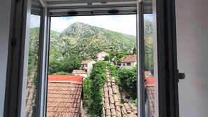 A view from a window with a mountain in the background, a red-tiled roof, and a stone wall. - Zukic Apartments RIsan  (Risan)