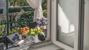 A window with a view of a balcony, a white table with a decorative mat, and a vase with flowers. - Zukic Apartments RIsan  (Risan)