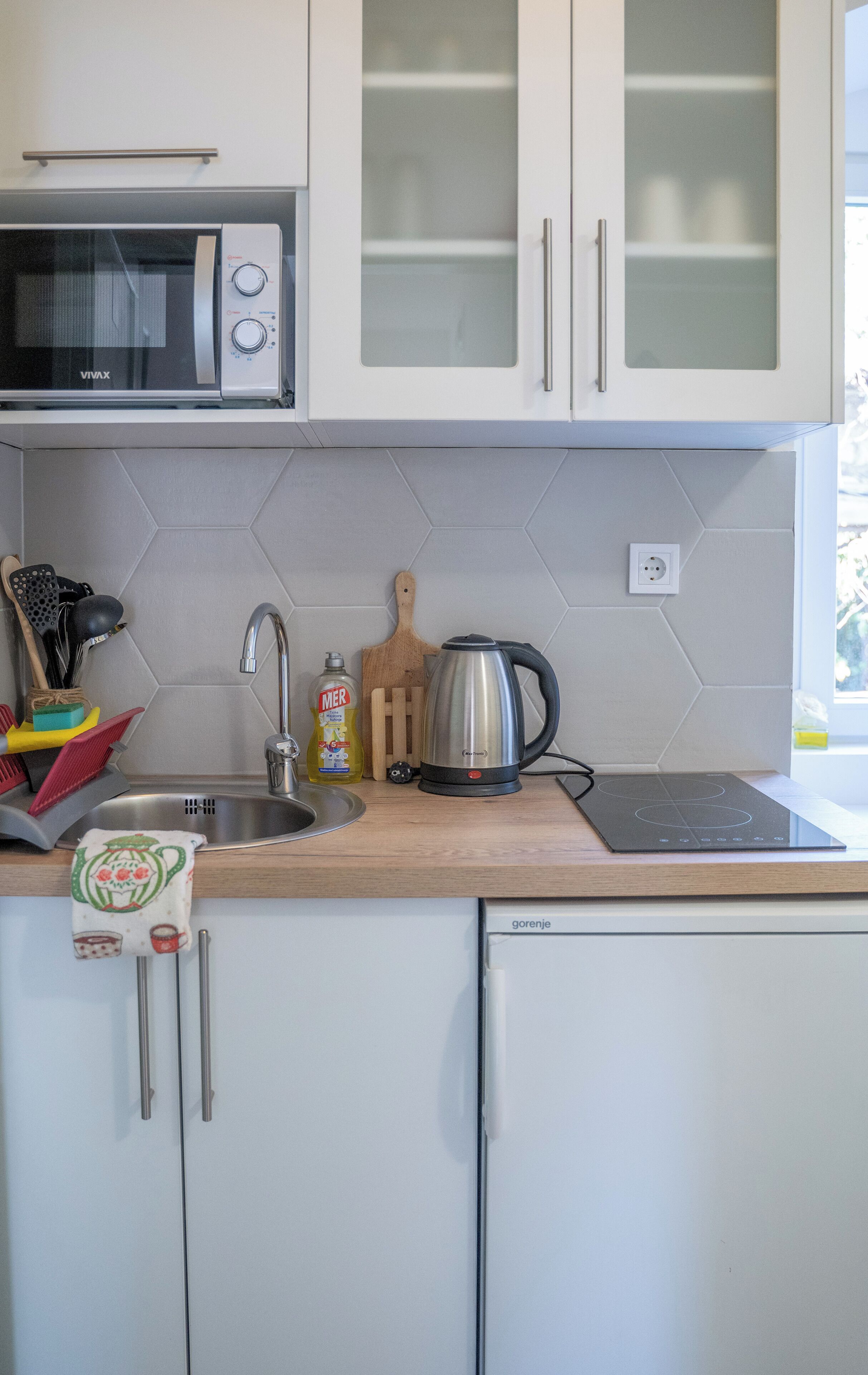 A kitchen with white cabinets, a microwave, a kettle, and a sink.