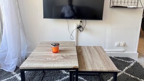 Uma sala de estar com televisão de tela plana na parede, uma pequena mesa de madeira com uma xícara e um tapete estampado.