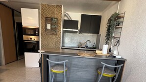 Uma cozinha compacta com uma ilha central, dois bancos altos e um forno embutido.