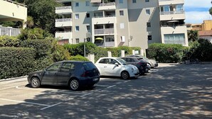Um edifício residencial com vários andares, varandas, carros estacionados e vegetação ao redor.