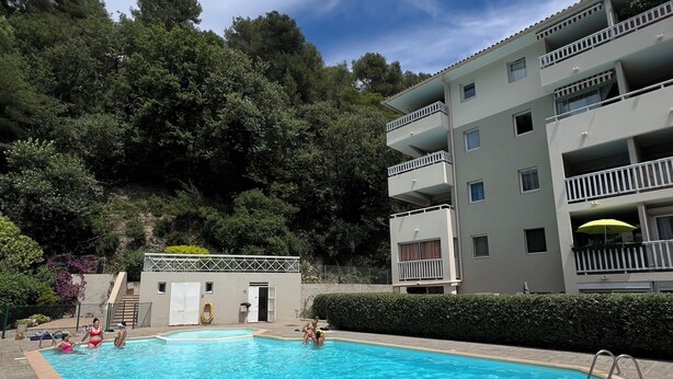 Uma piscina com deck revestido, rodeada por um edifício com várias andares e varandas.