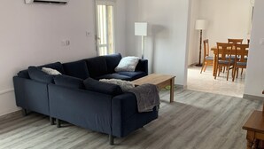 Un salon moderne avec un canapé bleu foncé, une table basse en bois et un coin repas comprenant une table et des chaises en bois.