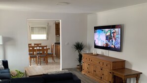 Un salon avec un canapé de couleur sombre, un fauteuil orange, un meuble en bois et un téléviseur fixé au mur.