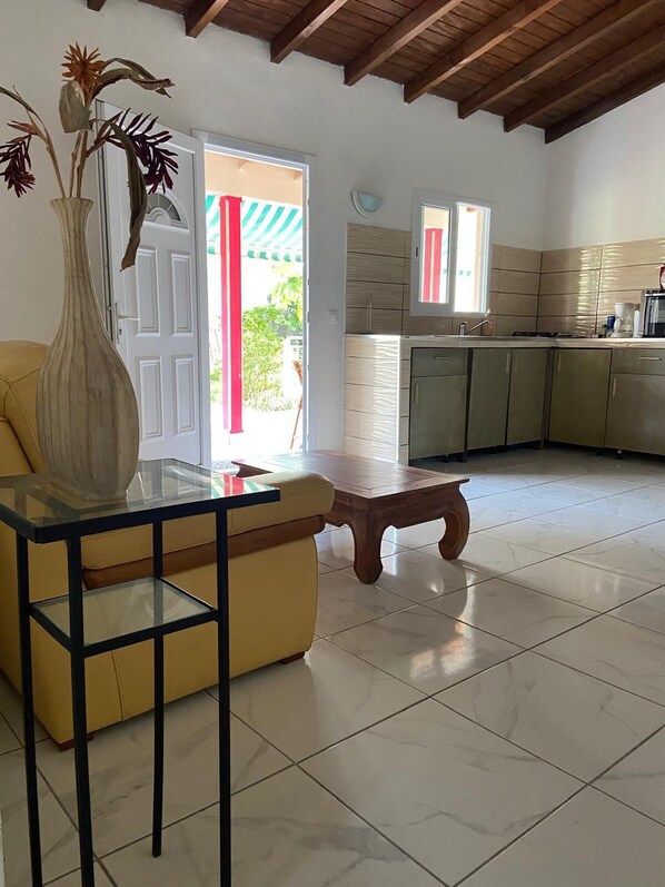 A modern kitchen with a built-in oven, a dining area with a yellow sofa and a glass-top table, and a view of the outdoors through a glass door.