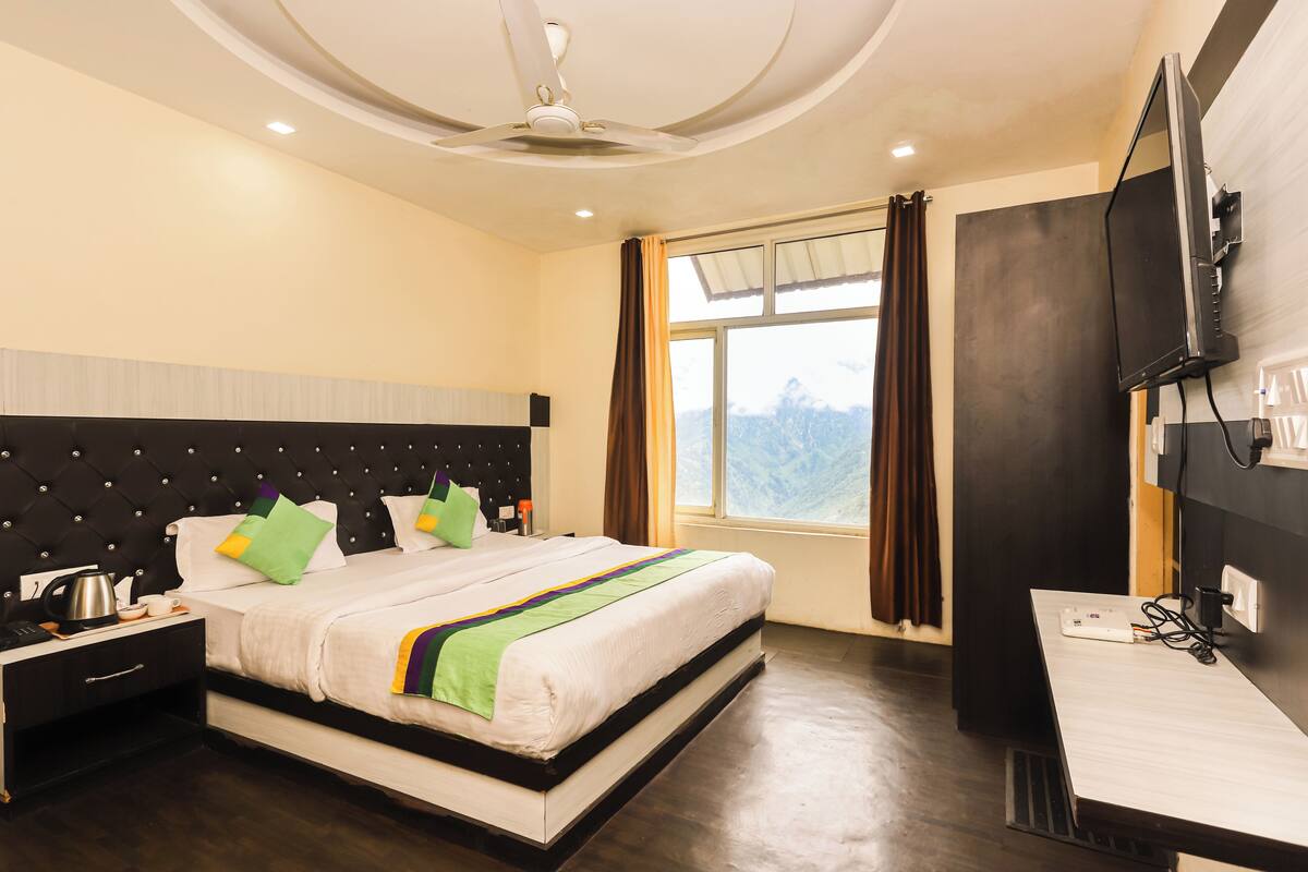 A hotel room with a bed, a desk, a TV, and a window with curtains.