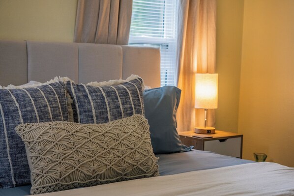 A neatly made bed with patterned pillows, a bedside lamp, and a window with curtains.