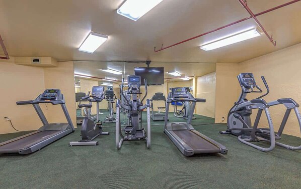 Un gimnasio con cintas de correr, elípticas y una pantalla de televisión.