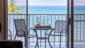 Un balcón con una mesa lista para dos personas, con vistas a una playa con palmeras y el océano.