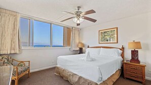 A bedroom with a large bed, a ceiling fan, a nightstand, a chair, and a window with a view.
