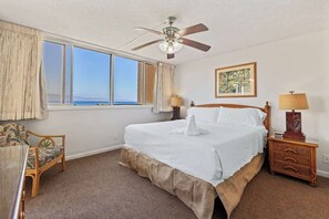 A bedroom with a large bed, a ceiling fan, a nightstand, a chair, and a window with a view.