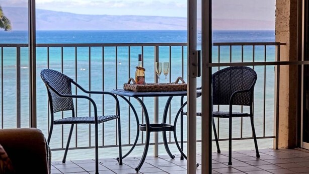 A balcony with a view of the ocean, two chairs, a table, and a bottle.