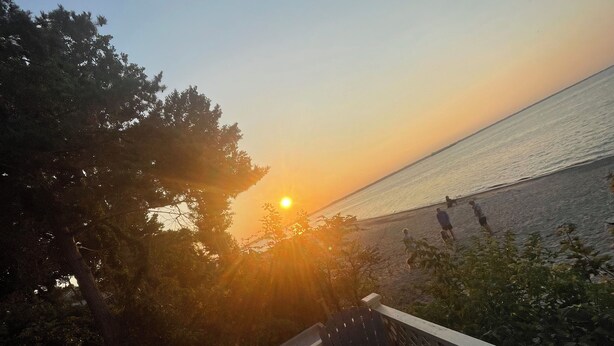 Une terrasse en bois avec des chaises, donnant sur une étendue d’eau au coucher du soleil.