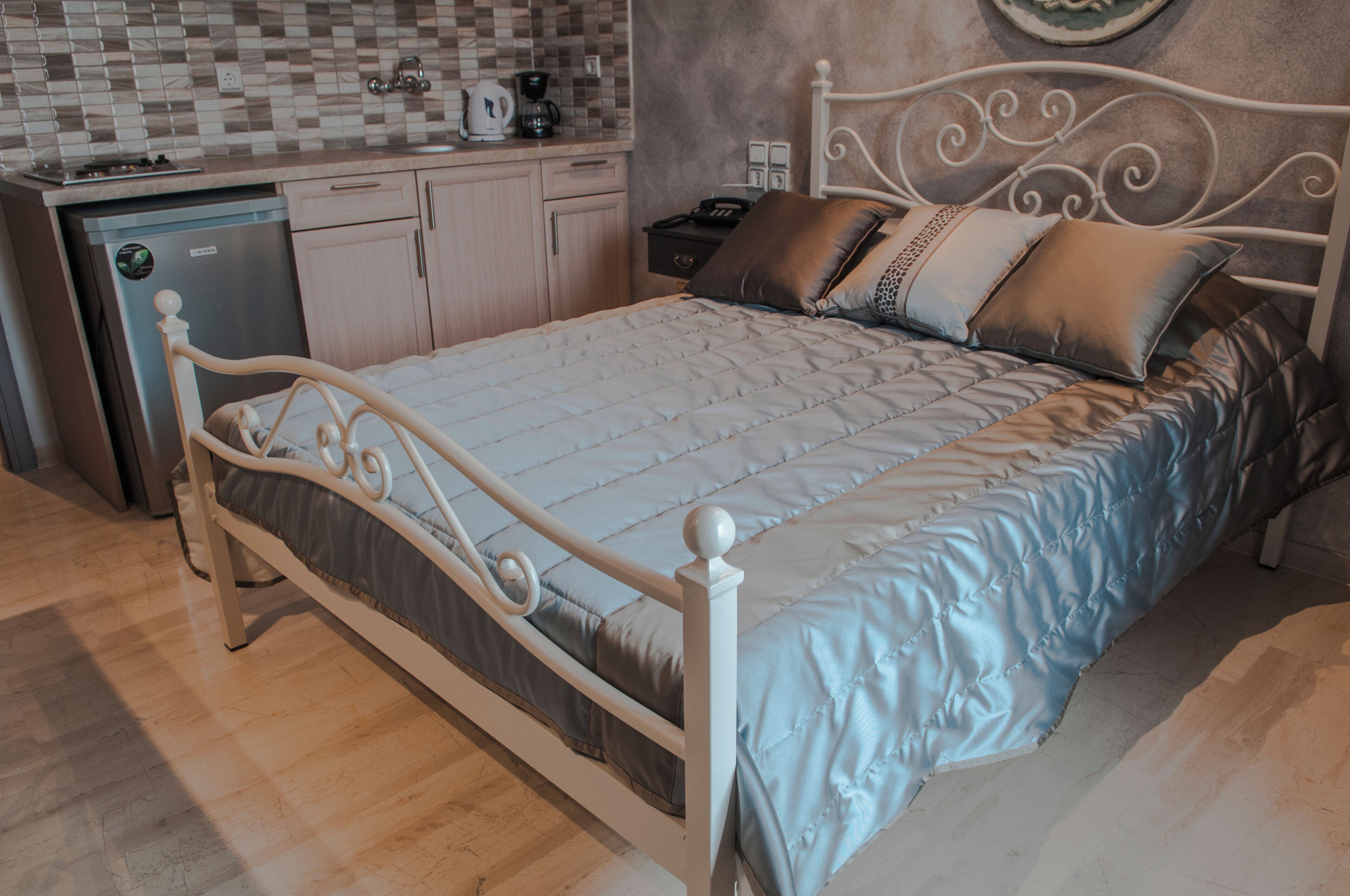 A bedroom with a bed, a bedside table, a nightstand, a wall-mounted clock, and a small cabinet.