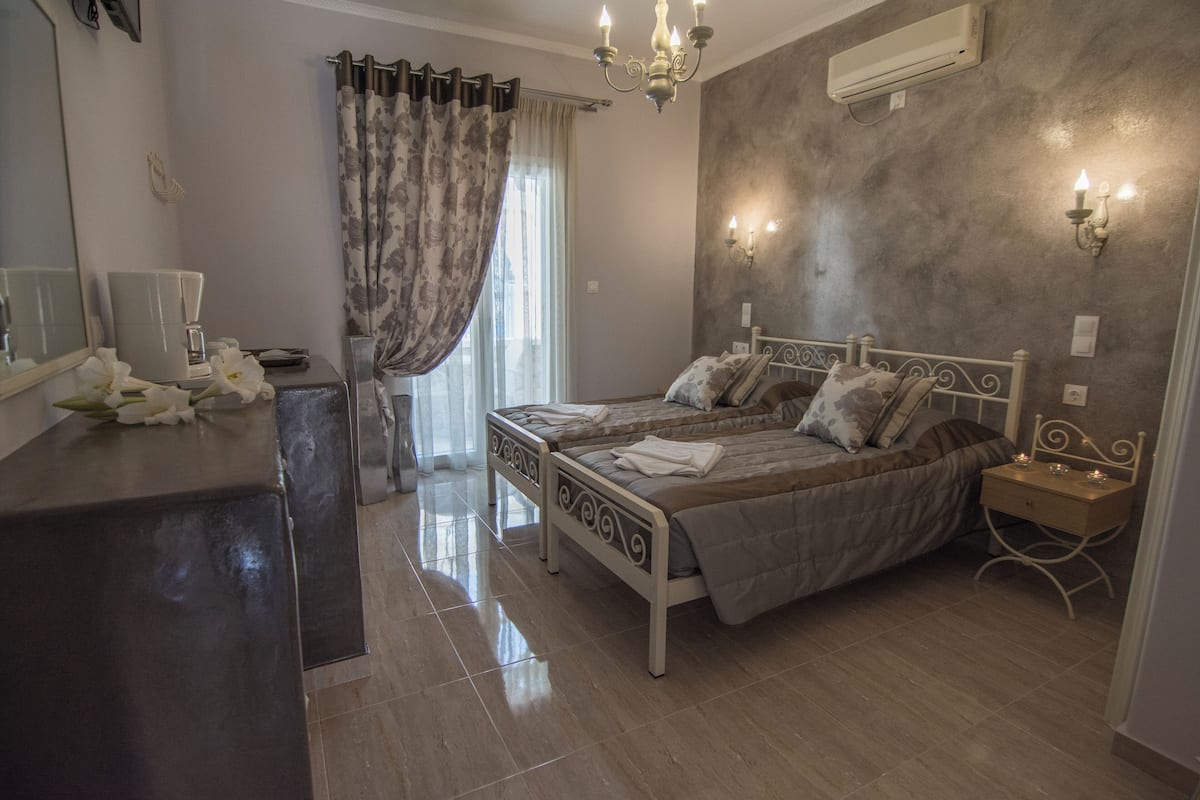 A bedroom with two beds, a bedside table, a dresser, a mirror, a chandelier, and an air conditioning unit.