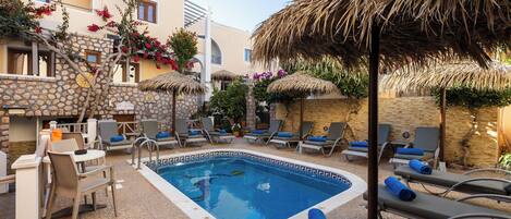 A swimming pool with lounge chairs and umbrellas, surrounded by stone walls and plants.