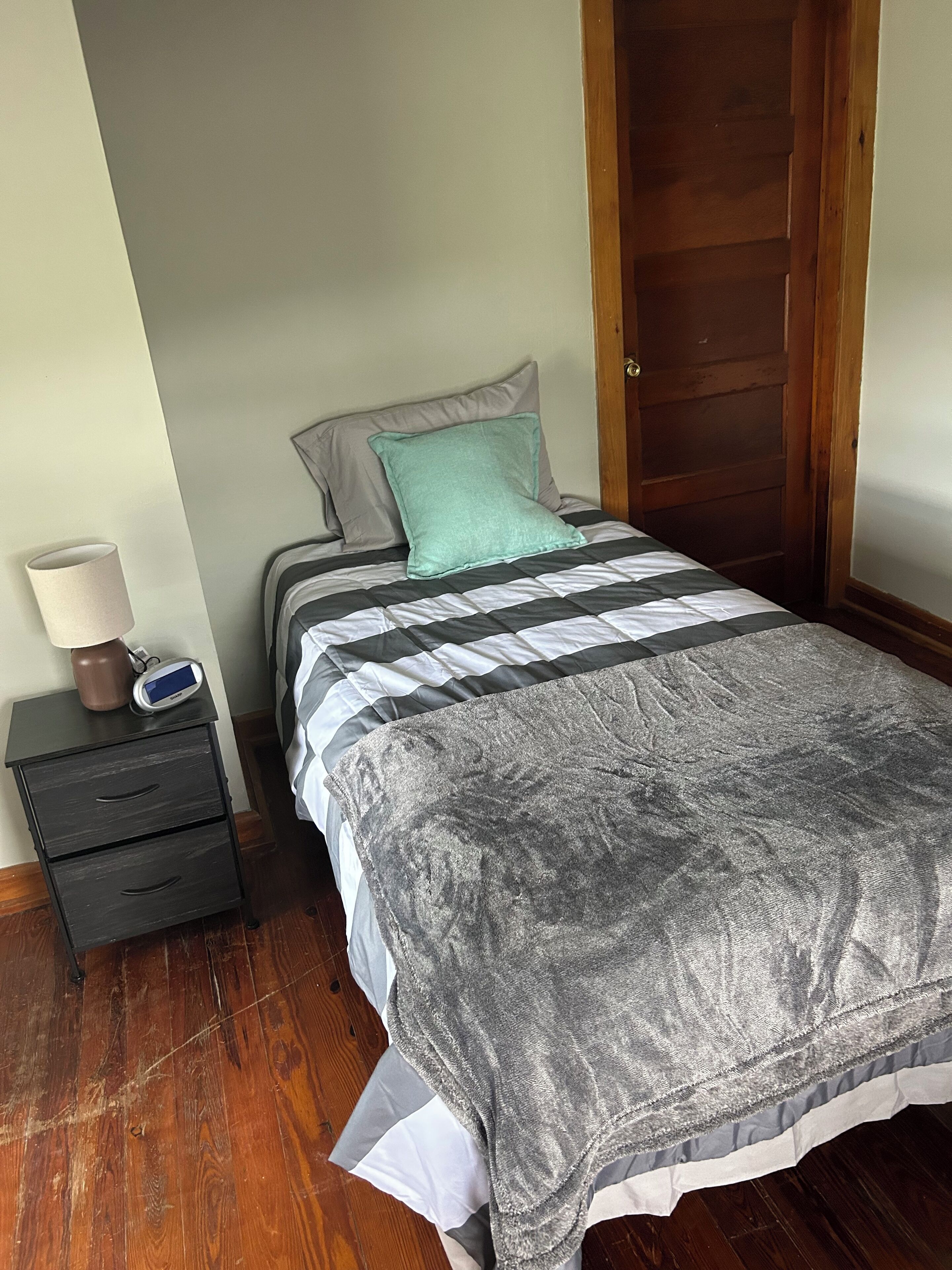 A bedroom with a bed, a nightstand, a lamp, and a wooden door.