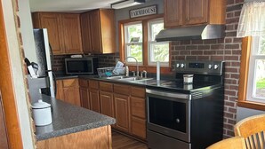 A kitchen with wooden cabinets, a farmhouse sign, a microwave, a stove, and a sink. - Cozy and Clean Farmhouse in Mountains near Gettysburg. No extra cleaning fees! (Orrtanna)