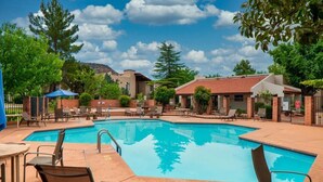 Una piscina con sillas de descanso y mesas, rodeada de árboles y edificios.