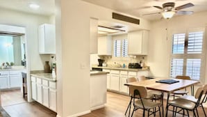 Una cocina moderna con armarios blancos, un comedor con mesa y sillas de madera, y un ventilador de techo.