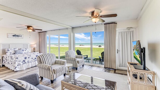 A spacious living room with a large bed, striped armchairs, a sofa, and a flat-screen TV.