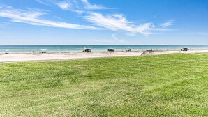 A beach with a grassy area in the foreground, a sandy beach, and a clear blue sky.