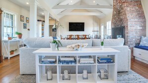 A modern living room with a grey sofa, white coffee table, and bookshelves. - Stunning Ocean View! Beachfront Nantucket Retreat (Nantucket)