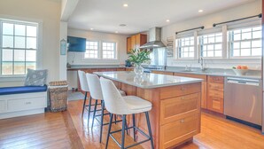 A modern kitchen with wooden cabinets, a large island with bar stools, and a built-in dishwasher. - Stunning Ocean View! Beachfront Nantucket Retreat (Nantucket)