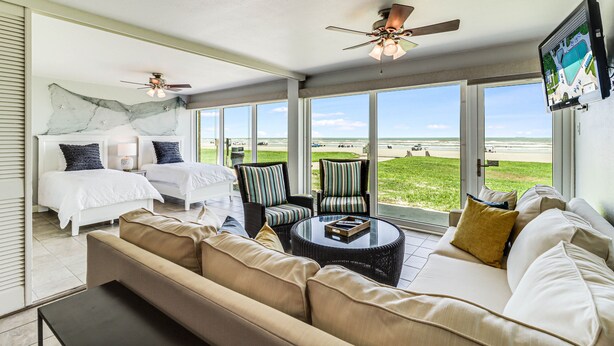 A spacious room with a large bed, two chairs, a sofa, and a ceiling fan. - Gulfstream Condos Unit 112 | Ground Floor | Gulf Front Views (Corpus Christi)