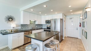 A modern kitchen with white cabinets, stainless steel appliances, a black countertop, and a tiled backsplash. - Gulfstream Condos Unit 112 | Ground Floor | Gulf Front Views (Corpus Christi)