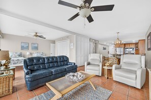 A living room with a blue sofa, a white armchair, a wooden coffee table, and a ceiling fan. - Gulfstream Condos Unit 115 | Gulf Front View | Beachfront Patio (Corpus Christi)