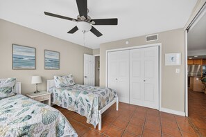 A bedroom with two beds, a ceiling fan, and a view into the kitchen. - Gulfstream Condos Unit 115 | Gulf Front View | Beachfront Patio (Corpus Christi)
