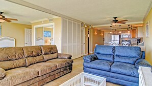 A living room with two sofas, a white coffee table, and a kitchen in the background. - Gulfstream Condos Unit 117 | Pool & Hot Tub | Beachfront Patio (Corpus Christi)