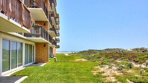 Un edificio moderno con un césped, vistas a la playa y cielo despejado.