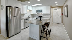 Una cocina moderna con armarios blancos, electrodomésticos de acero inoxidable, una isla central con taburetes e iluminación empotrada en el techo.