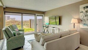 Una sala de estar con un sillón verde, un sofá color beige y un televisor en la pared.