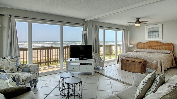A spacious room with a large bed, a television, and a balcony with a view of the ocean. - Gulfstream Condos Unit 205 | Corner Unit with Beachfront Balcony (Corpus Christi)