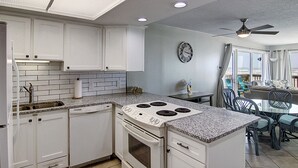 A modern kitchen with white cabinets, a granite countertop, a built-in oven, and a dining area with a table and chairs. - Gulfstream Condos Unit 205 | Corner Unit with Beachfront Balcony (Corpus Christi)