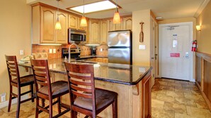 A kitchen with wooden cabinets, a stainless steel refrigerator, a microwave, and a large island with bar stools. - Gulfstream Condos Unit 208 | Pool & Hot Tub | Private Balcony, Panoramic View (Corpus Christi)