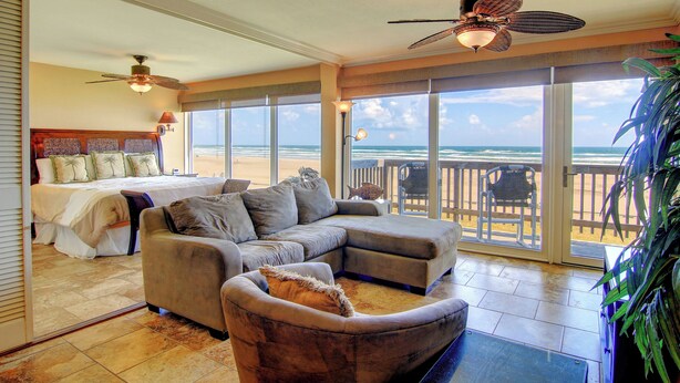 A spacious living area with a large sectional sofa, a ceiling fan, and a view of the ocean through large sliding glass doors. - Gulfstream Condos Unit 208 | Pool & Hot Tub | Private Balcony, Panoramic View (Corpus Christi)