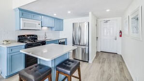 Une cuisine moderne avec des meubles bleus, un plan de travail blanc, des appareils en acier inoxydable et un tabouret de bar.