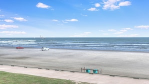 Une plage avec un ciel dégagé, une route bordée de glissières de sécurité et quelques véhicules sur le sable.
