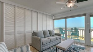 A balcony with a grey sofa, a small table, and a ceiling fan. - Gulfstream Condos Unit 212 - Beach Front View & Balcony (Corpus Christi)