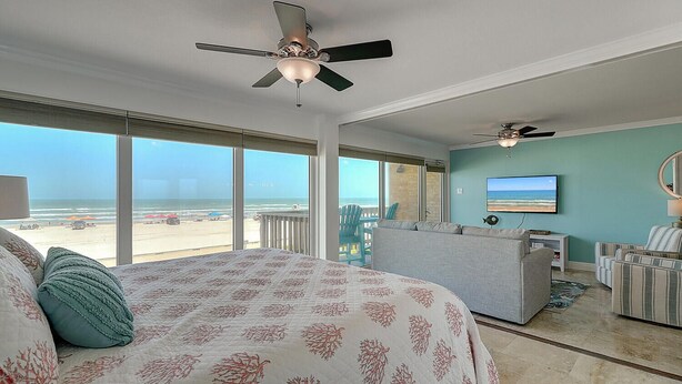 A bedroom with a large bed, a ceiling fan, a TV, and a view of the beach. - Gulfstream Condos Unit 212 - Beach Front View & Balcony (Corpus Christi)