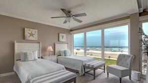 Un dormitorio con dos camas, ventilador de techo, vista a la playa y una silla.