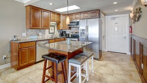 Una cocina con armarios de madera, un refrigerador de acero inoxidable, una encimera de granito y un taburete de bar.